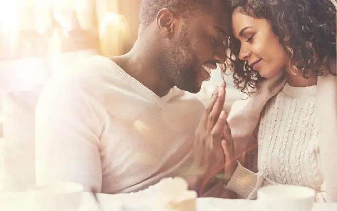 A couple enjoying a tender and affectionate moment, gently touching hands and smiling at each other with a warm, golden light surrounding them, under the guidance of a Sexual Health Expert in Los Angeles.