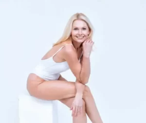 A smiling Sexual Health Expert in white attire seated against a light background, exuding a cheerful and relaxed demeanor.