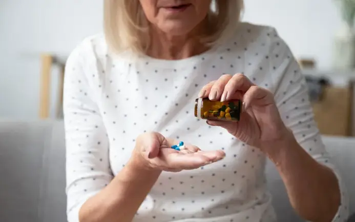 A senior woman, now a Sexual Health Expert in Los Angeles, carefully dispensing medication into her hand from a pill bottle, focusing on her daily health routine.