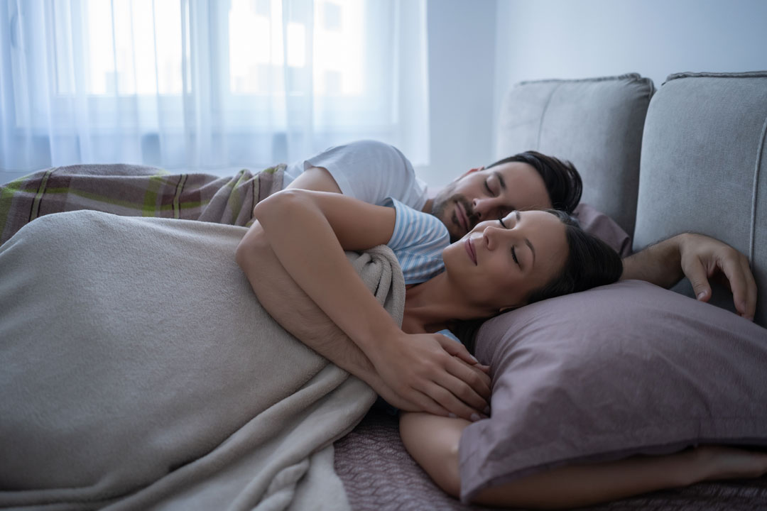 A couple sleeping peacefully, snuggled together on a couch under a cozy blanket, after consulting with a sexual health specialist in Los Angeles.