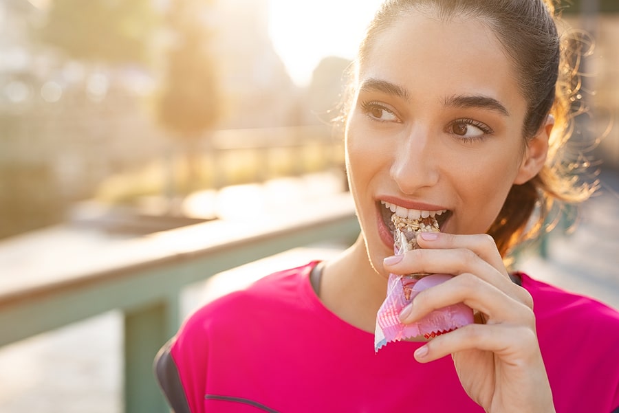 Active lifestyle - woman enjoying a healthy snack bar during a sunny outdoor workout break, revitalized by advice from a hormone therapy Los Angeles expert.