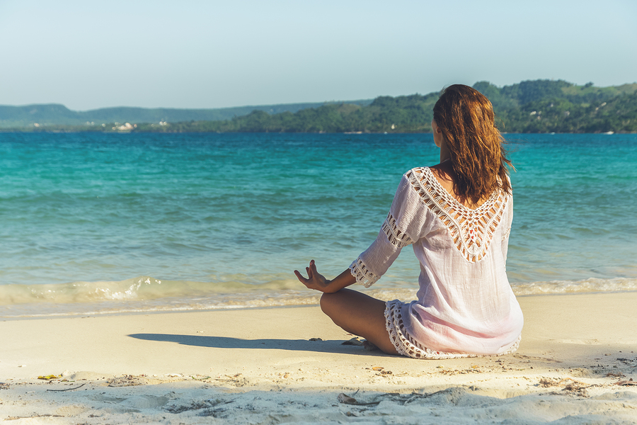 A serene moment on the beach: a person in a relaxed pose practicing meditation by the tranquil blue sea, finding peace during their journey with hormone therapy in Los Angeles.
