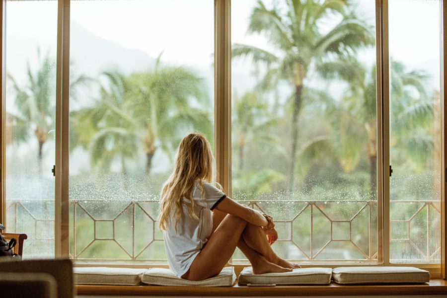 A person in contemplation, gazing out of a rain-spattered window at a serene tropical landscape, reflects on their journey with hormone therapy in Los Angeles.
