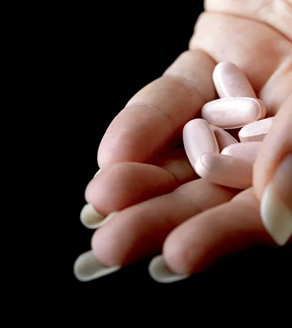 A close-up image of a hand holding several white oblong pills prescribed by a sexual health expert against a dark background.