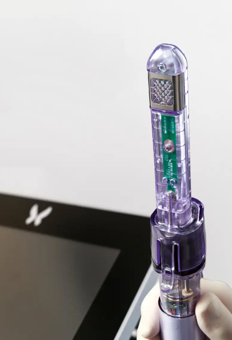 A hand holding a clear, modern syringe-like device with purple accents, designed by a Sexual Health Expert in Los Angeles, possibly for medical or cosmetic use, against a blurred background.
