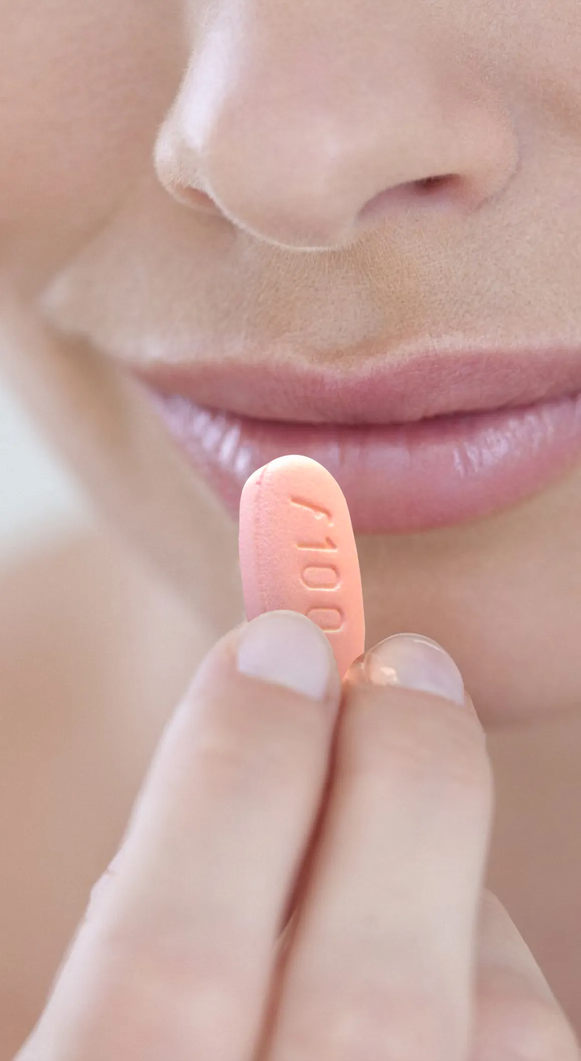 A Sexual Health Expert in Los Angeles holding a pink pill close to their lips, possibly about to take medication.