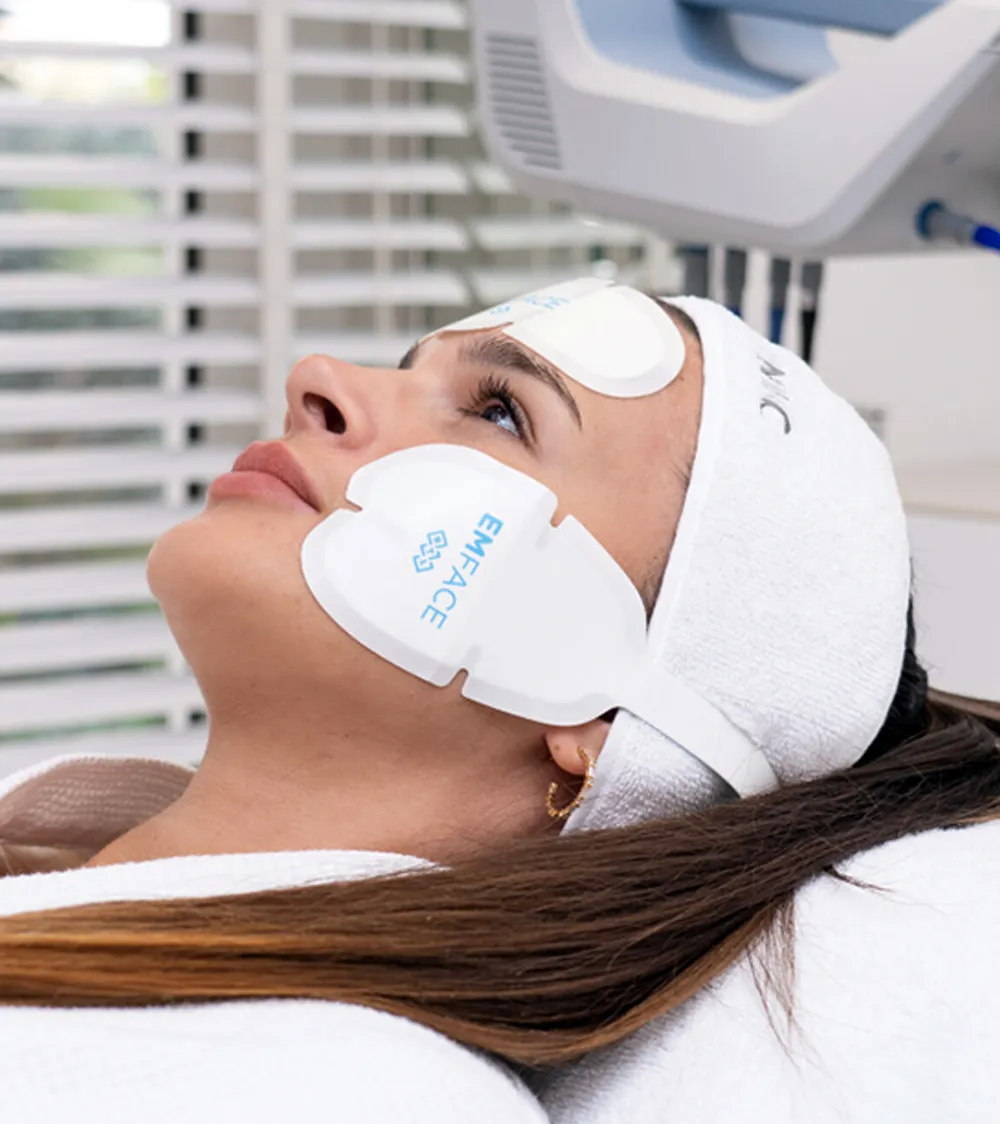 Woman undergoing a facial skincare treatment with protective eye patches and a headband, relaxing at a beauty clinic supervised by an expert in sexual health.