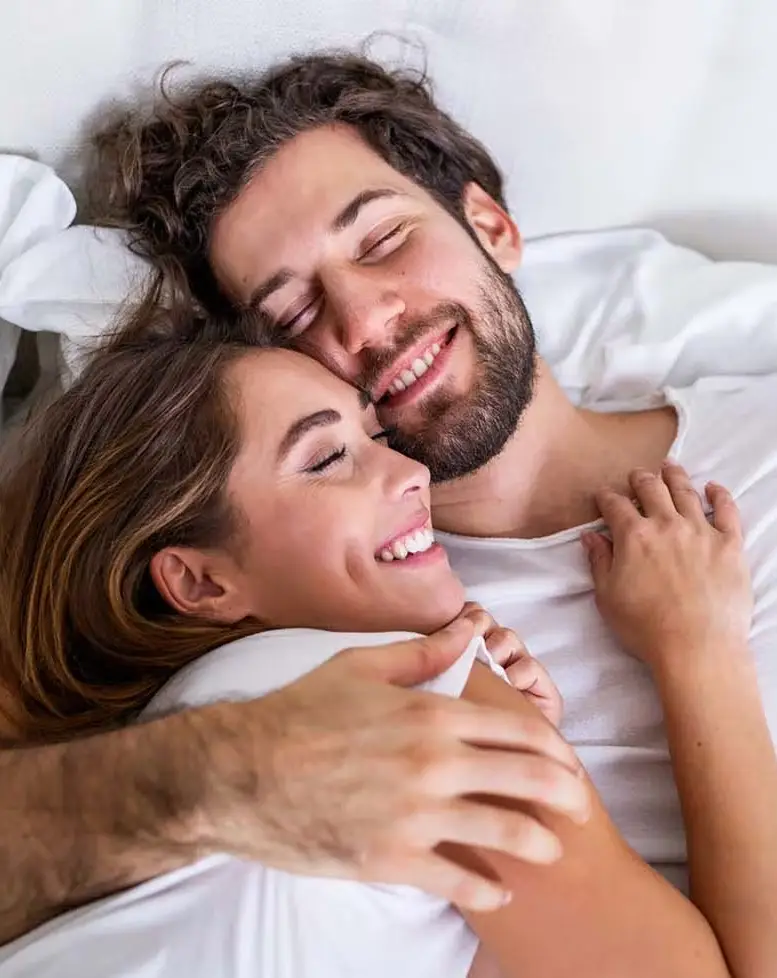 A moment of tenderness: a smiling couple embracing in bed, basking in shared affection and contentment, guided by a Sexual Health Expert in Los Angeles.