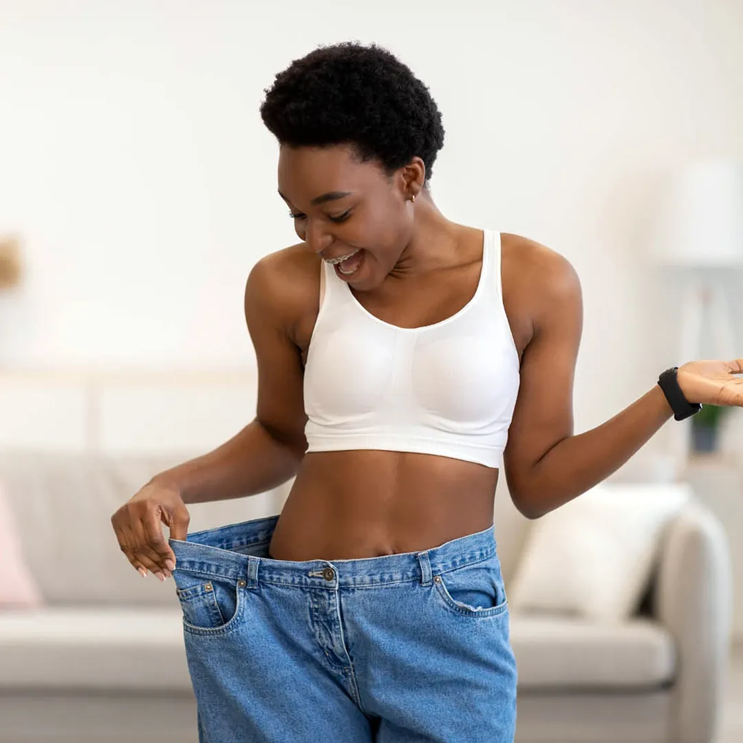 A joyful woman, now a sexual health expert in Los Angeles, celebrates her weight loss by showing how much her jeans have loosened.