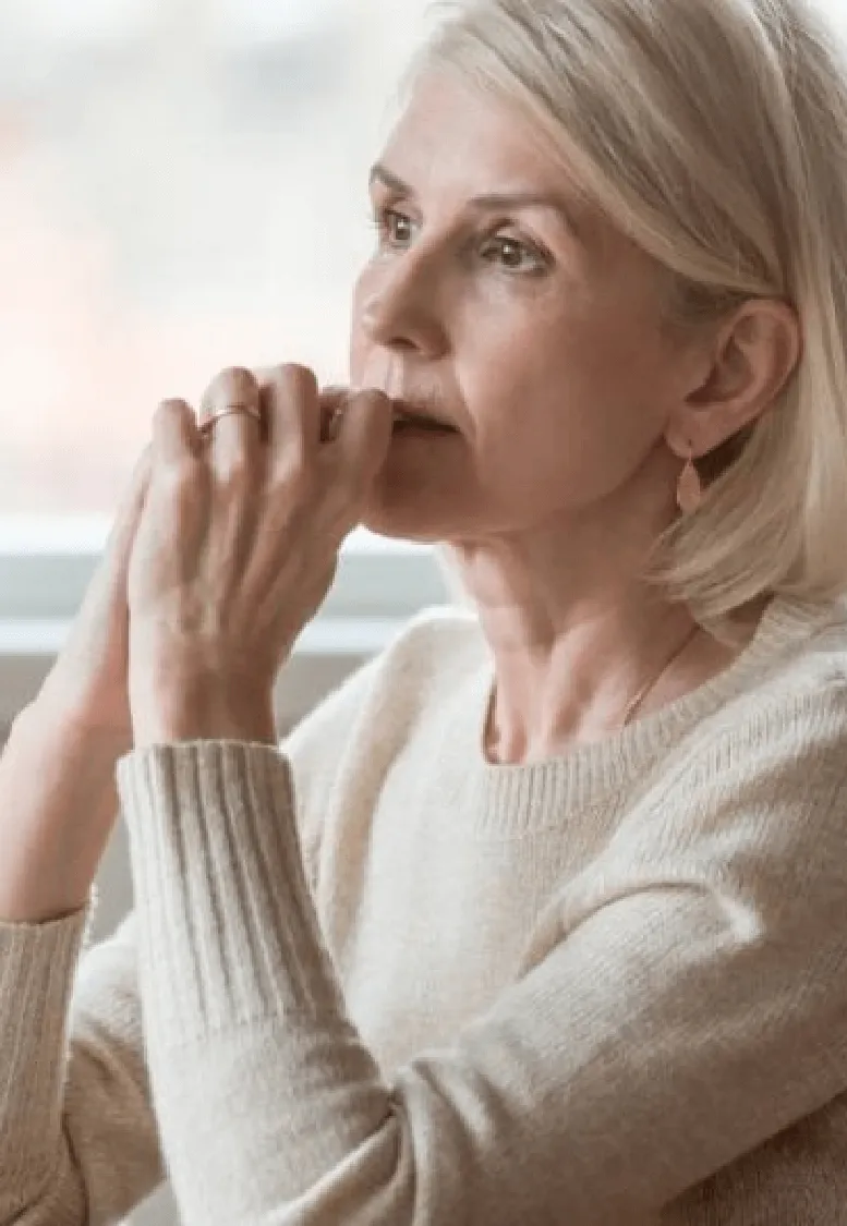 A contemplative senior woman, a Sexual Health Expert in Los Angeles, with her hand on her chin, lost in thought and gazing into the distance.