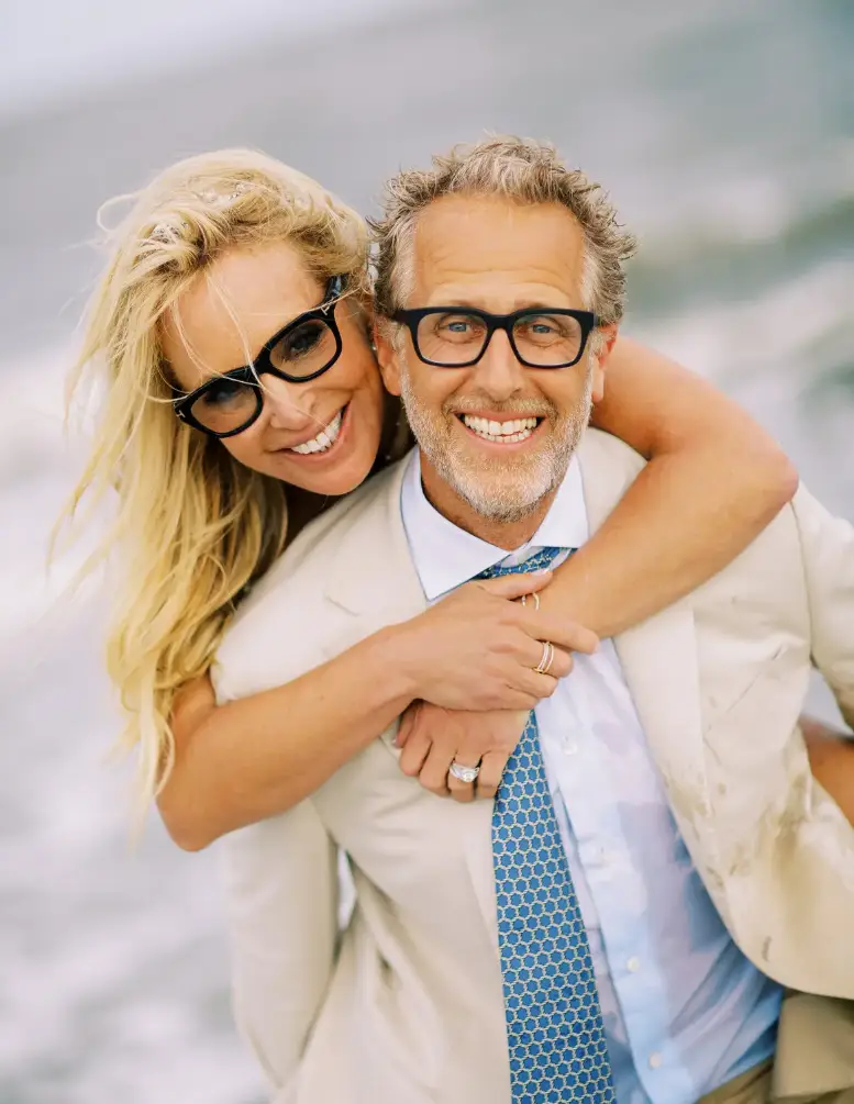 A joyful couple embracing and smiling on the beach, showcasing a moment of happiness and togetherness against a soft-focused coastal backdrop, reminiscent of advice from a Sexual Health Expert in Los Angeles.